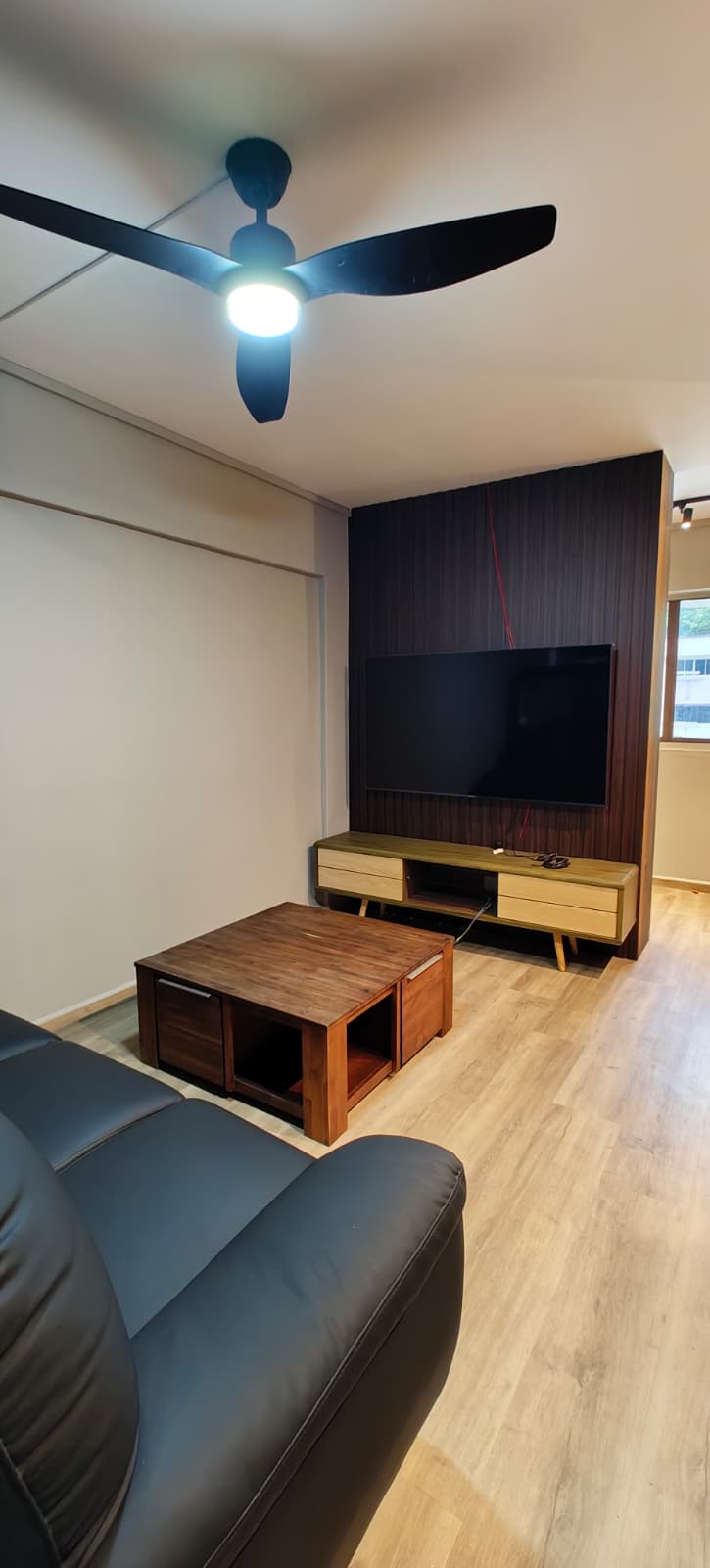 Living room with dark leather sofa, timber coffee table and dark slatted TV feature wall